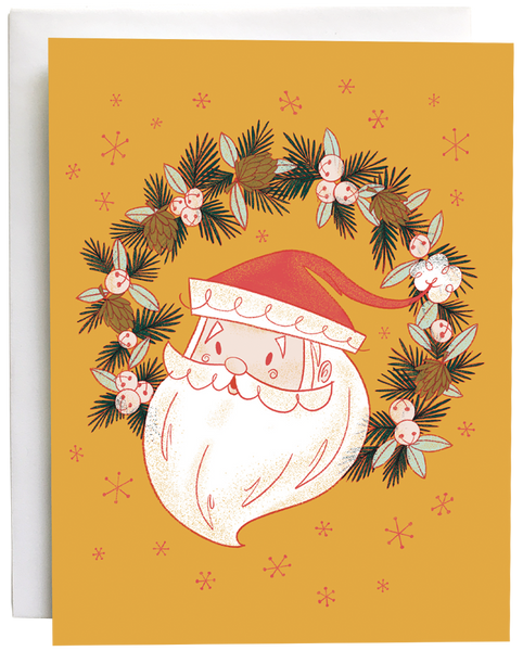 A yellow card shows a midcentury-style illustration of Santa's head in a wreath of jingle bells, pinecones and evergreen branches. The card is against a white envelope on a white background.